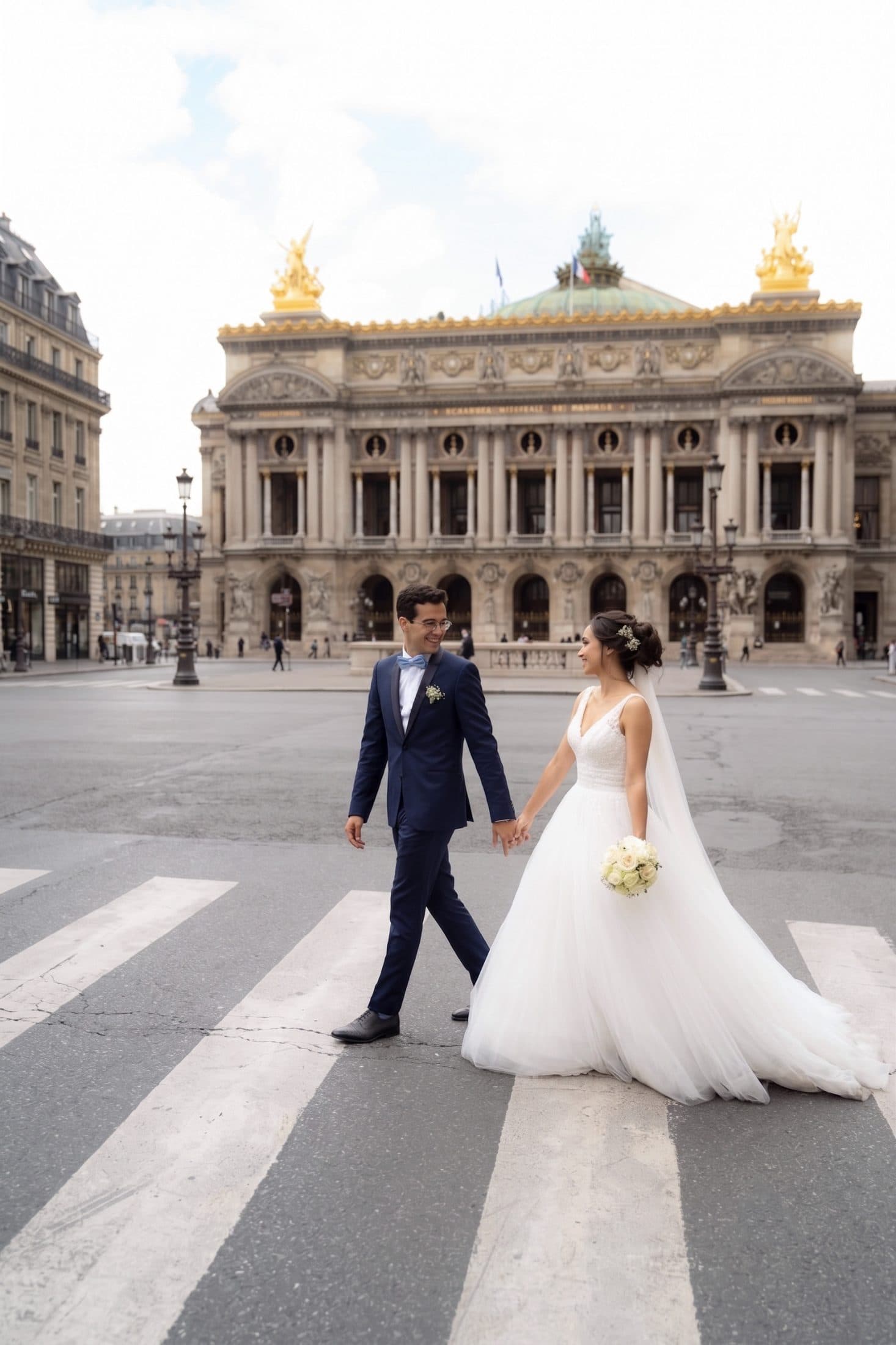 Bride and groom holding hands while crossing the street in front of the Palais Garnier Opera House in Paris.