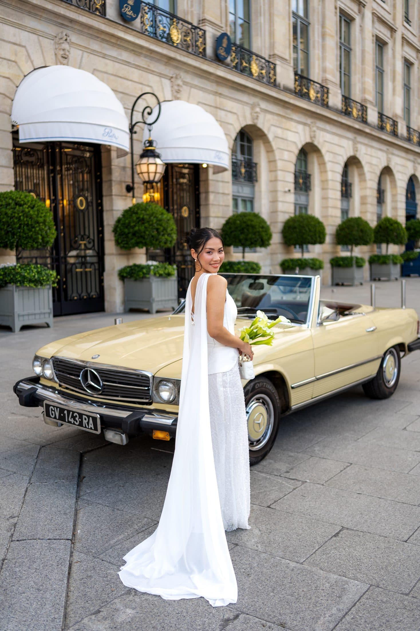 Bride in a white gown posing by a vintage convertible car during an elopement photoshoot in Paris.